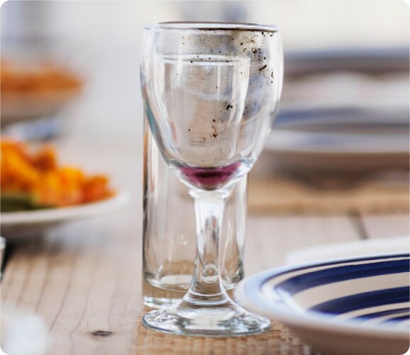 Copa de cristal sucia junto a un vaso y algunos platos.
