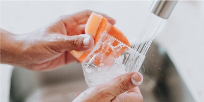 Manos lavando vaso de cristal con jabón y Esponja Cero Rayas de Scoth-Brite.