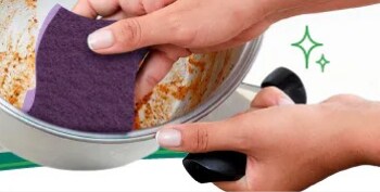 Mano limpiando una olla con una Fibra Esponja Scotch-Brite® Extrema para remover residuos adheridos.
