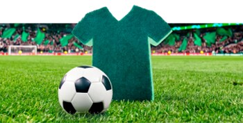 Balón de fútbol sobre césped frente a una esponja edicón especial, con un estadio desenfocado al fondo.
