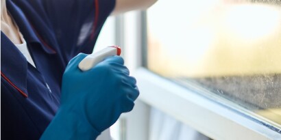 Mano con guante azul esparciendo solución de limpieza con un atomizador.
