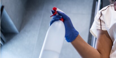 Mano con guante azul sosteniendo un atomizador para limpiar superficies.
